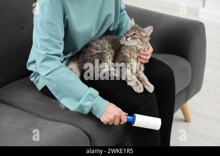 Distacco di animali domestici. Donna con rullo di pelucchi che rimuove i capelli di gatto dai pantaloni sul divano a casa, primo piano Foto Stock