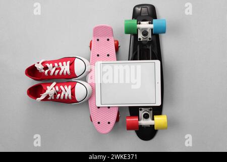 Tablet, skateboard e scarpe moderni su sfondo grigio chiaro, con disposizione piatta. Spazio per il testo Foto Stock