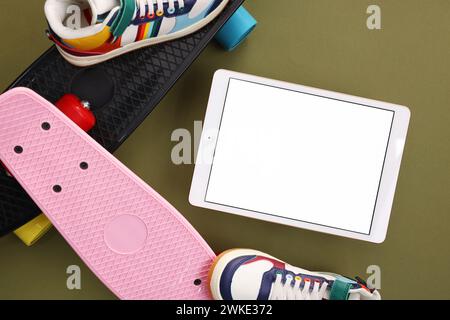 Tablet moderno, skateboard e scarpe su sfondo verde oliva, piatto. Spazio per il testo Foto Stock