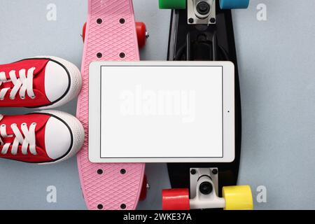 Tablet, skateboard e scarpe moderni su sfondo grigio chiaro, con disposizione piatta. Spazio per il testo Foto Stock