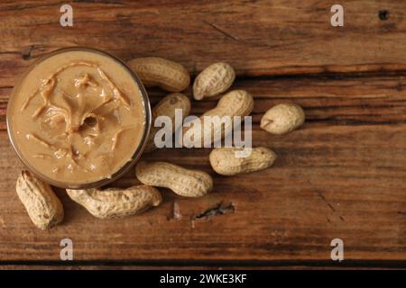 Delizioso burro di noci nel recipiente e arachidi su un tavolo di legno, vista dall'alto Foto Stock