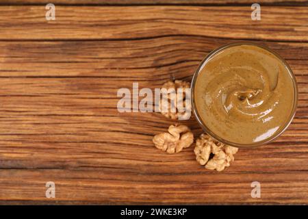 Delizioso burro di noci nel recipiente e noci sul tavolo di legno, vista dall'alto. Spazio per il testo Foto Stock