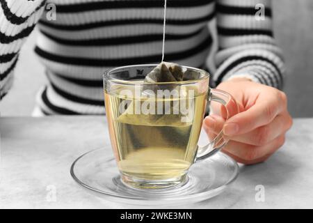 Preparazione del tè. Donna che mette la bustina di tè nella tazza al tavolo leggero, primo piano Foto Stock