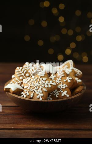 Gustosi biscotti di Natale con glassa nel recipiente su un tavolo di legno contro le luci sfocate Foto Stock