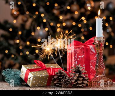 Composizione natalizia con candele in fiamme, regali e coni sullo sfondo di un albero di Natale decorato e scintillanti in fiamme. Foto Stock