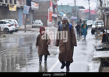 Srinagar, India. 18 febbraio 2024. A Srinagar, Kashmir, India, il 18 febbraio 2024: Un padre e un figlio passeggiano per le strade piovose, indossate dai tradizionali ferri, mentre la regione celebra una tempestiva e rinfrescante pioggia. Sullo sfondo di tratti superiori carichi di neve, una previsione meteorologica promette un paesaggio invernale stravagante, con forti nevicate previste dal 18 al 20 febbraio. (Foto di Danish Showkat/Sipa USA) credito: SIPA USA/Alamy Live News Foto Stock