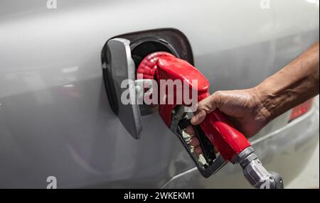 Primo piano della mano di un uomo che usa una pompa di benzina per riempire la sua auto di carburante. Un uomo riempie la sua auto con una benzina al distributore di benzina. Messa a fuoco selettiva, copia Foto Stock