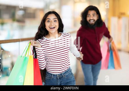 Eccitata giovane donna indiana che corre per centro commerciale, tira il suo ragazzo Foto Stock