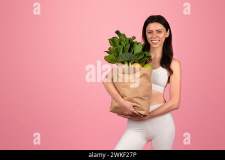 Concetto di stile di vita sano con una giovane donna allegra in abbigliamento atletico bianco che tiene in mano una borsa della spesa Foto Stock