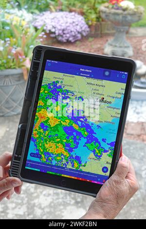 Donna con le mani in mano Apple ipad pro tablet app di allarme pioggia e dati radar a colori in tempo reale strato di pioggia mappa locale meteo umido sulla finestra di Essex Regno Unito Foto Stock