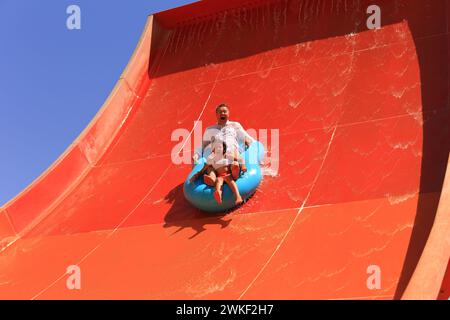 Famiglia che scende su uno scivolo d'acqua in un parco acquatico in estate. Padre e figlia piccola cavalcano su anelli gonfiabili in vacanza al mare. Estate Foto Stock