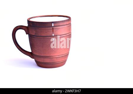 L'immagine mostra un bicchiere di argilla marrone con il latte versato al suo interno e gocce di latte sulle pareti del contenitore. Foto Stock