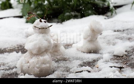 piccolo piccolo pupazzo di neve bianco due occhi e volto felice sorriso felice neve inverno sorriso da occhi bastoncini di piccoli ciottoli pupazzo di neve in miniatura dalla neve primaverile Foto Stock