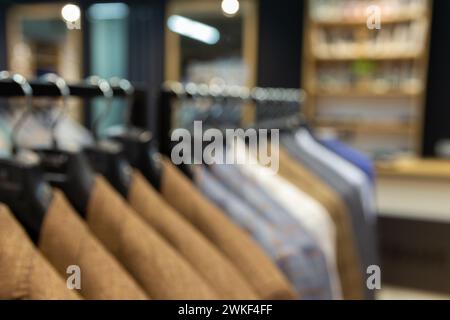 Sfondo sfocato con abiti da uomo, giacche appese su un rack per la visualizzazione. Eleganti giacche da uomo appese in fila Foto Stock