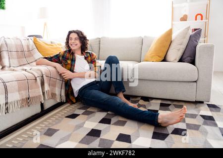 Foto di un ragazzo di buon umore positivo indossa una camicia a quadri sul pavimento seduto godendo del fine settimana in casa camera Foto Stock