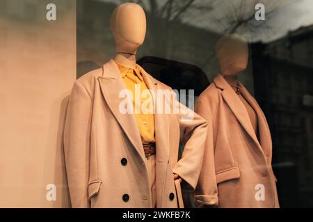 Manichini in una vetrina con abiti stagionali. Cappotto beige e camicia giallo brillante. Foto Stock