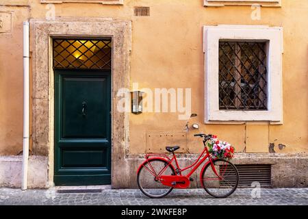 Immagine di una bicicletta rossa in una vecchia e stretta strada acciottolata a Roma, Italia. La vecchia strada di Roma, Italia. Architettura e punto di riferimento di Roma. Foto Stock