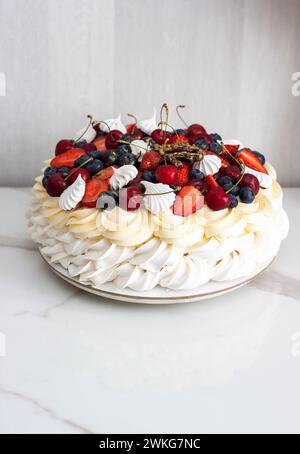 Torta Pavlova con formaggio cremoso montato, salsa al cioccolato, fragole fresche, mirtilli e lamponi, decorata con meringhe su sfondo semplice Foto Stock