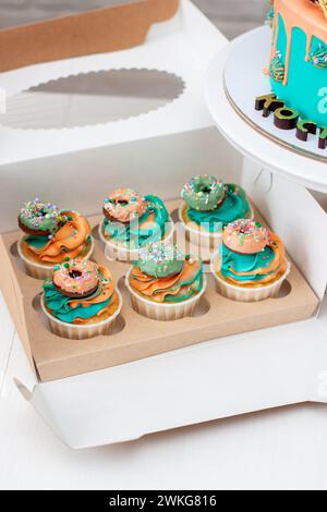 Deliziosi cupcake di compleanno su due lati, realizzati nei colori verde e arancione, riccamente decorati con ciambelle e lecca lecca Foto Stock