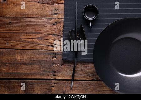 Wok del ferro vuoto, ciotola per salsa e bacchette su un tavolo di legno, piano. Spazio per il testo Foto Stock