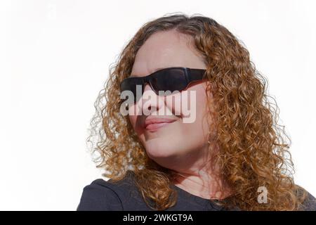 Donna bionda dai capelli ricci vista di profilo con occhiali da sole con sfondo bianco e spazio per le copie Foto Stock