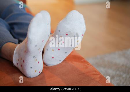 una persona si sta sdraiando su un divano con i piedi in alto e indossa calze a pois bianche Foto Stock