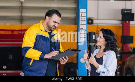 Le donne del cliente sono contente dell'elenco di controllo dell'assistenza auto dei lavoratori meccanici nell'officina del centro auto Foto Stock