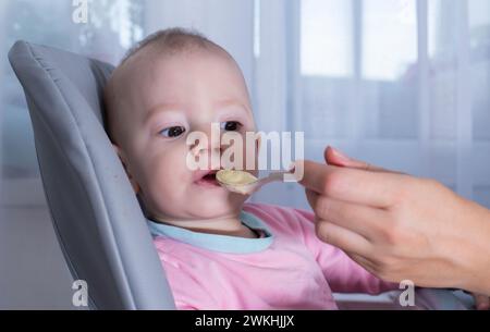 La mano della madre nutre il porridge di zucca del bambino. Ritratto di un bambino di un anno, primo piano. Spazio di copia per il testo Foto Stock