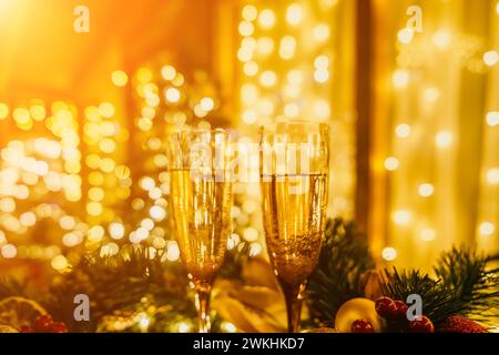 Due bicchieri di champagne ripieni di champagne sono collocati su un tavolo vicino all'albero di Natale. Gli occhiali sono circondati da luci che creano un'atmosfera festosa Foto Stock