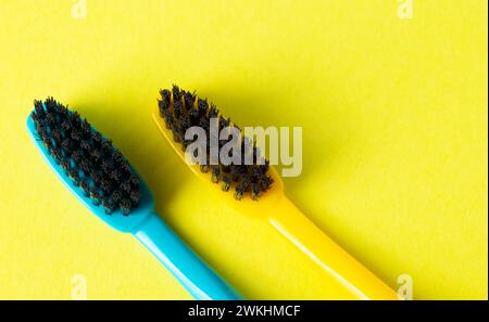 Due spazzolini con setole nere dure al carbone su sfondo giallo, primo piano. Il concetto di igiene e pulizia dei denti in odontoiatria. Copia spac Foto Stock