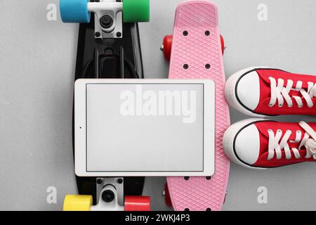 Tablet, skateboard e scarpe moderni su sfondo grigio chiaro, con disposizione piatta. Spazio per il testo Foto Stock