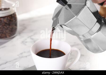 Versare caffè aromatico dalla moka alla tazza sul tavolo di marmo bianco, primo piano Foto Stock