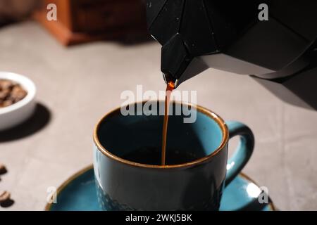 Versare caffè aromatico dalla moka alla tazza al tavolo leggero, primo piano Foto Stock