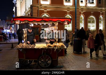 Istanbul, Turchia - 11 dicembre 2023: Le ragazze locali comprano mais e castagne arrosto in strada a tarda sera. Piccola profondità di campo, concentrati su una ragazza f Foto Stock