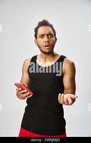 confuso bell'afroamericano che tiene il telefono e guarda la macchina fotografica, scommesse online Foto Stock