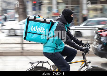 Belgrado, Serbia - 20 febbraio 2024: Servizio di corriere Wolt con una borsa di consegna in bicicletta in una strada trafficata piena di pedoni, vista profilo Foto Stock