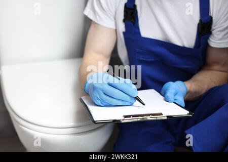 L'idraulico scrive i risultati dell'esame della ciotola del water e del primo piano Foto Stock