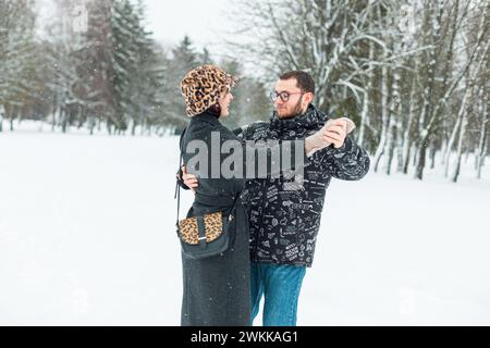 Giovane e bella coppia di amanti della moda in eleganti abiti invernali che ballano in un parco invernale con la neve Foto Stock