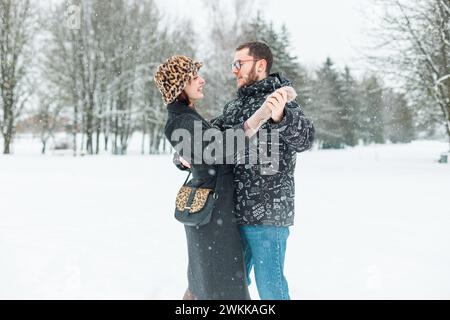 Felice bella giovane divertente coppia di amanti in abiti invernali alla moda ballando in un parco con la neve. Amore, sentimenti e danza Foto Stock