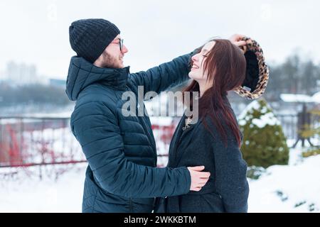 Bella coppia di giovani amanti alla moda in abiti invernali alla moda per strada. bel ragazzo mette un cappello sulla ragazza e sorride, divertiti Foto Stock