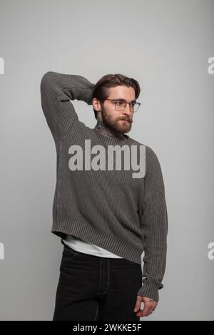 Bel giovane, elegante uomo d'affari di successo, hipster, con occhiali alla moda con acconciatura e barba in un elegante maglione vintage a maglia in resina Foto Stock