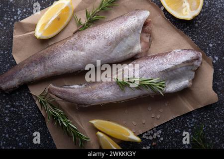 Pesce crudo fresco adornato con limone e rosmarino, presentato su uno sfondo scuro e strutturato, perfetto per temi culinari e contenuti gastronomici Foto Stock