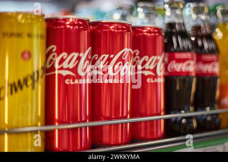 Scaffale in negozio con bibite di marche diverse. Coca Cola, schweppes. Lattine in alluminio e bottiglie in vetro di varie dimensioni. Editoriale sulle bevande, popolare carboidrati Foto Stock