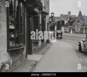 Una Cotwold Street degli anni '1950 con vetrine sulla baia e una Morris 8 degli anni '1950 che passa oltre. Questa immagine è stata presa dalla foto originale. Foto Stock