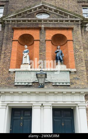 Staues di pietra di Coade al di fuori dell'ex Bluecoat Charity School di St Johns Old School House, Scandrett Street, Wapping, Londra, E1, Inghilterra, Regno Unito Foto Stock