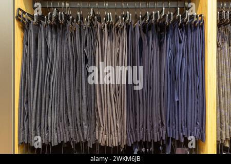 Pantaloni classici da uomo con appendiabiti in una boutique. Mostra molti pantaloni da uomo appesi su grucce in magazzino su grucce in un negozio di abbigliamento maschile. Foto Stock