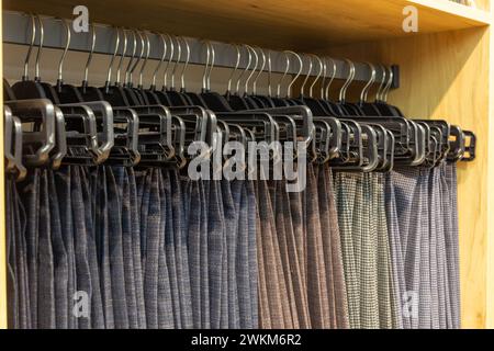 Pantaloni classici da uomo con appendiabiti in una boutique. Mostra molti pantaloni da uomo appesi su grucce in magazzino su grucce in un negozio di abbigliamento maschile. Foto Stock