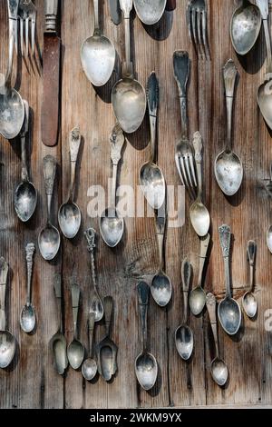 Argenteria vintage assortita appesa su pareti in legno. Collezione di cucchiai e forchette antichi. Arredi in stile rustico e tradizione culinaria Foto Stock