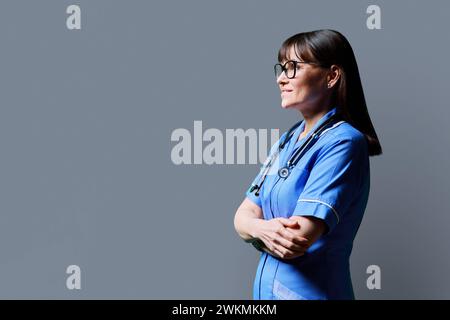 Ritratto di un'infermiera sicura di mezza età che guarda in profilo su sfondo grigio in studio Foto Stock