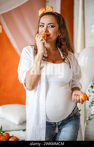 Donna incinta che mangia mandarini nella sua camera da letto a casa. Mangiare sano durante il concetto di gravidanza. Foto Stock